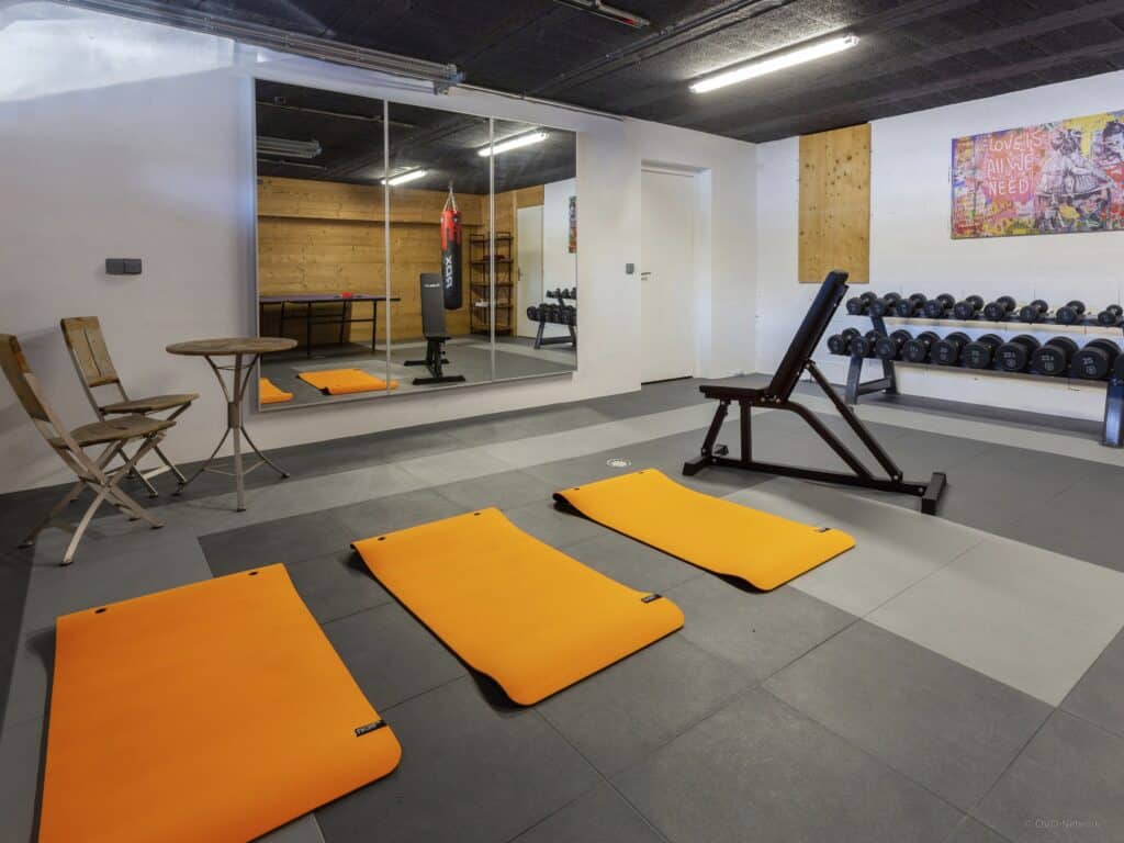A fitness studio with bright orange mats, a large mirror, punching bag, weight bench and stand and table for resting.