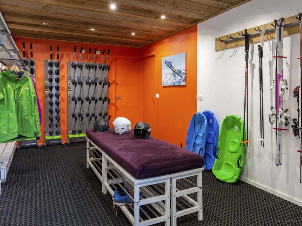 The ski room at Chalet Le Mousqueton which has a bright orange wall, central bench and plenty of hanging space.