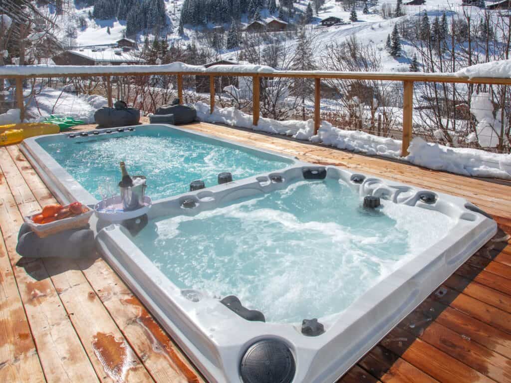 An outdoor swim spa with adjoining hot tub photographed in the snow.