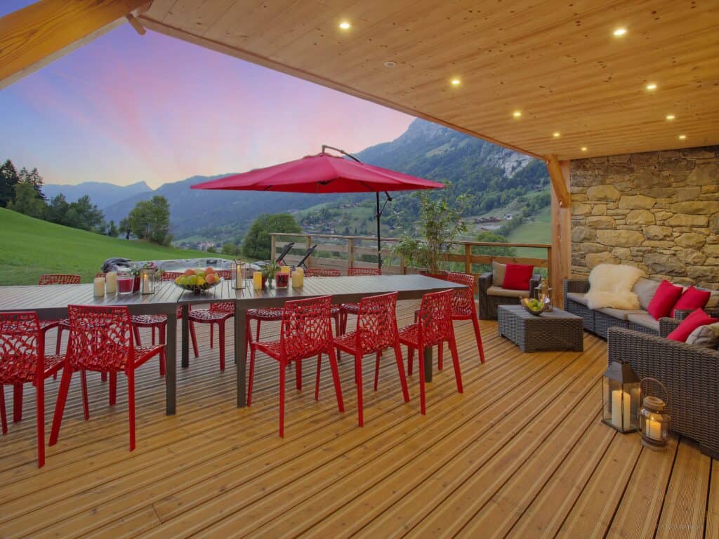 Chalet Le Buhel's outdoor dining area with red chairs and a parasol