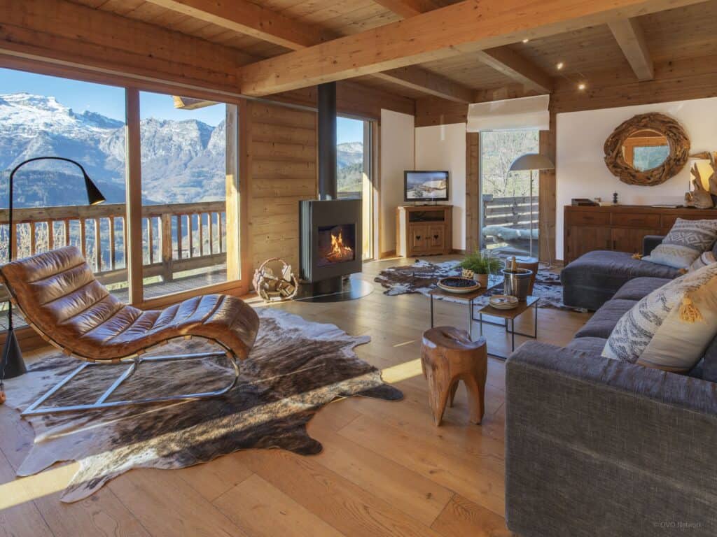 Salon de chalet avec cheminée allumée et vue sur les montagnes.