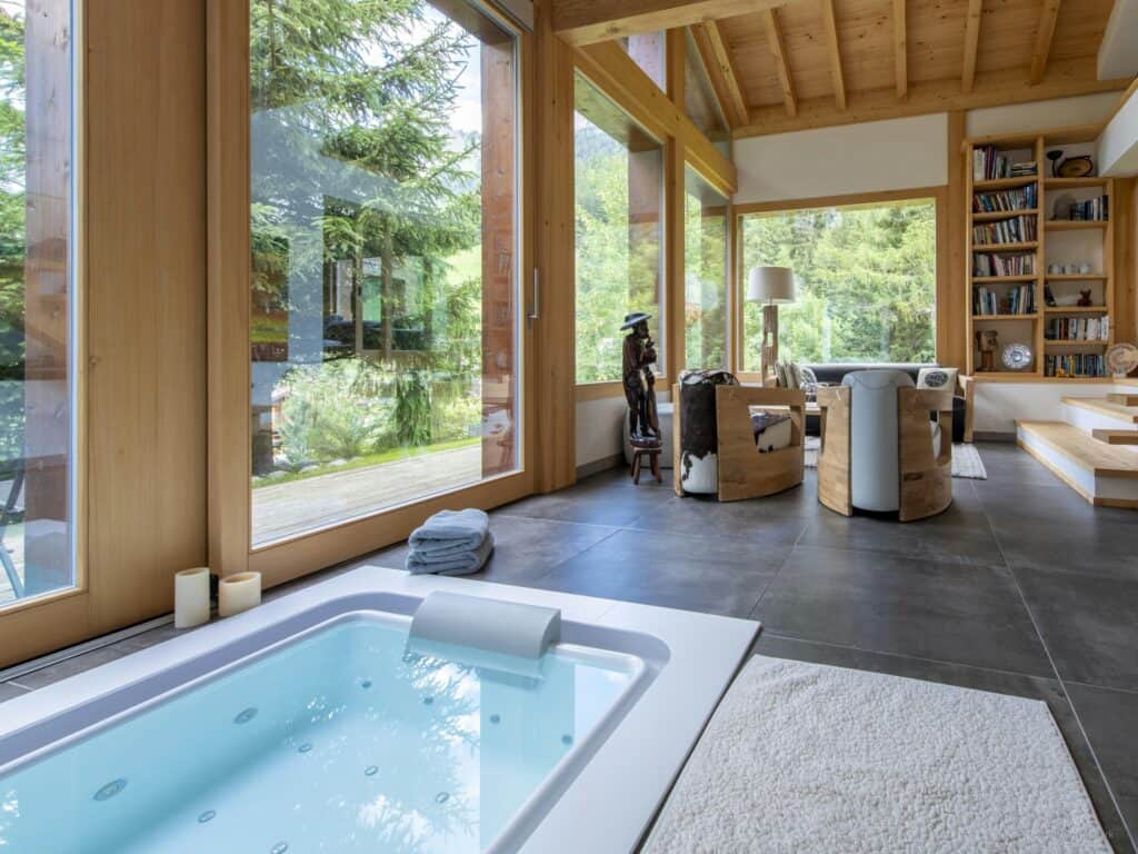 Élégant salon et jacuzzi intérieur avec vue sur une forêt alpine.