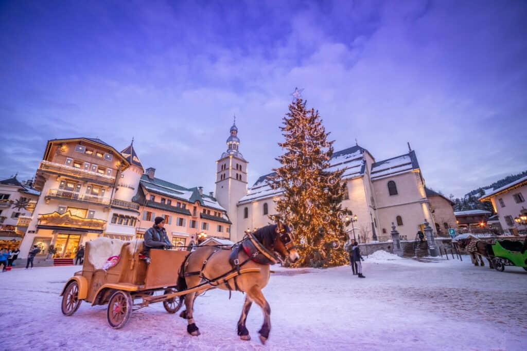A horse-drawn carriage in snow Megève, with a Christmas tree in the background