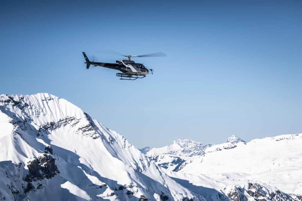 A helicopter flies over the snow peaks of the Alps