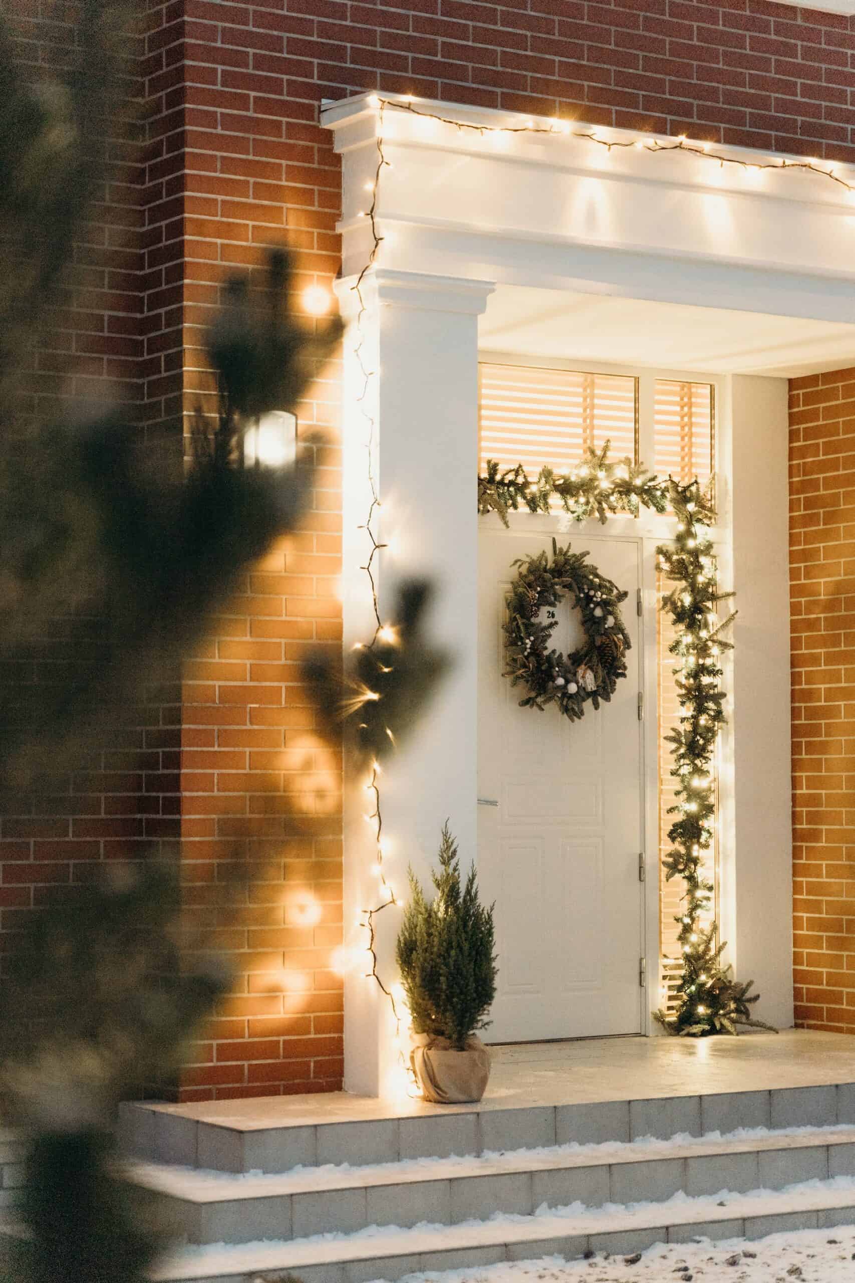 A white front door decorated with a traditonal fir wreath, a garland and some white lights