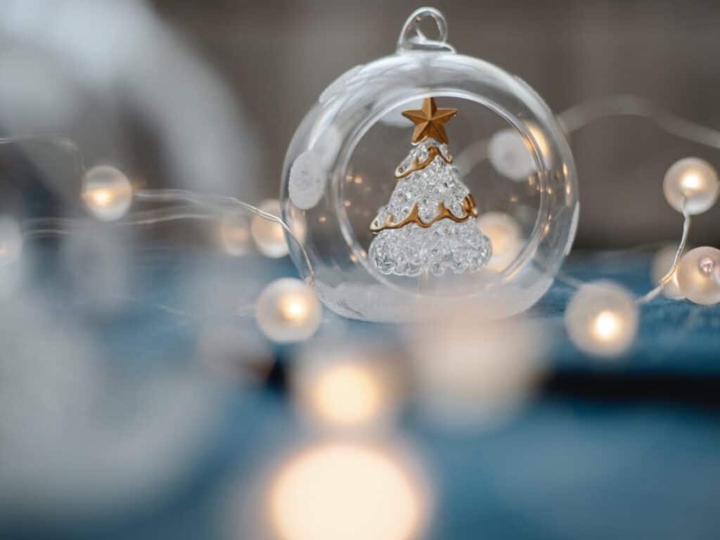 Guirlande argentée et lumineuse et boule de Noël en verre avec sapin de Noël à l'intérieur.