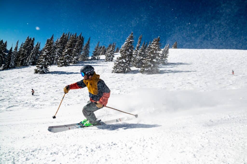 Un homme faisant du ski avec des arbres en arrière plan et un beau ciel bleu. 
