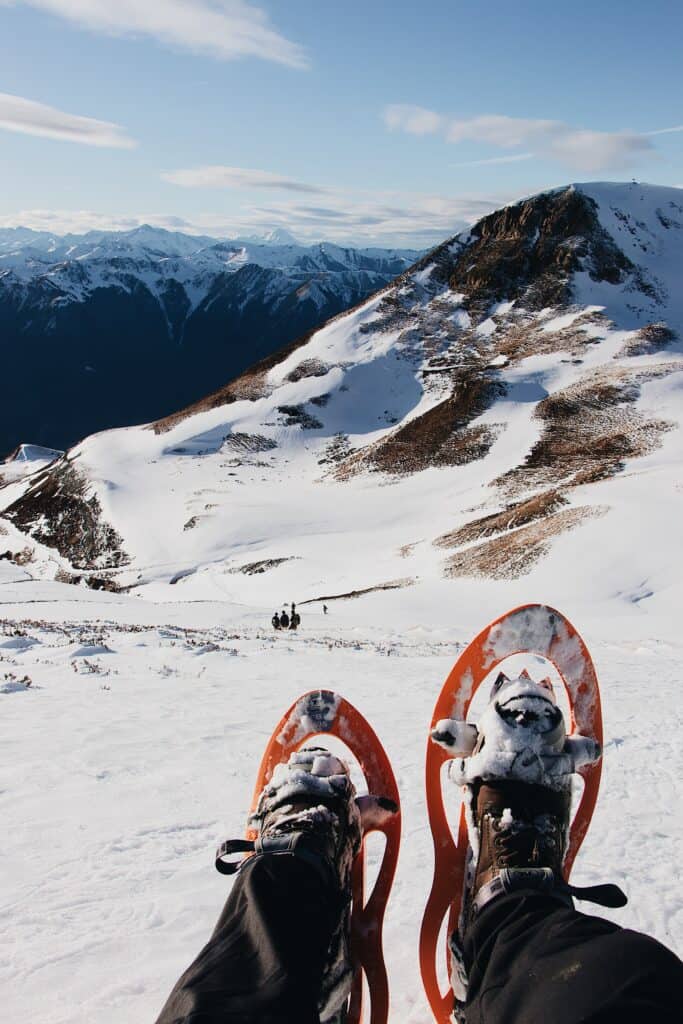 Pieds chaussés de raquettes de neige et paysage montagneux en arrière plan. 