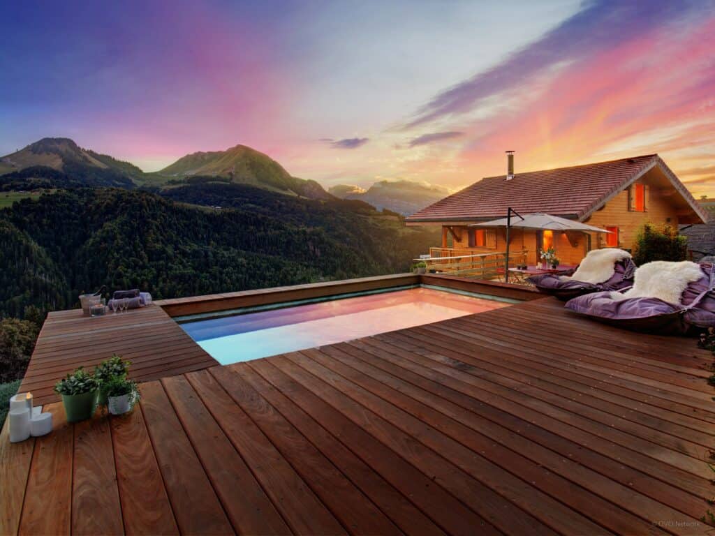 Chalet au crépuscule avec piscine extérieure entourée d'une terrasse en bois et vue sur la montagne
