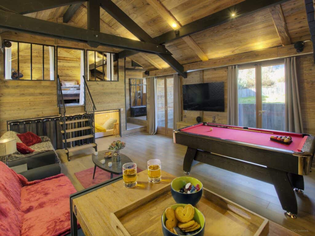 Red pool table, sofas and TV screen with a bedroom in the background.