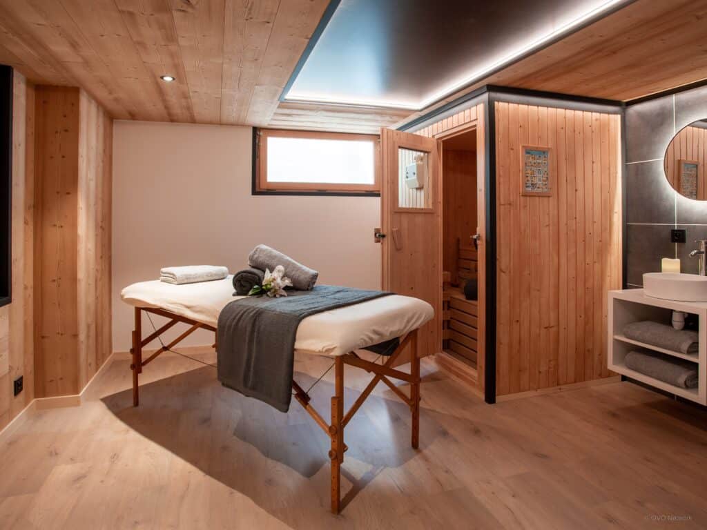 Salle de spa avec une table de massage et des serviettes pliées disposées sur la table, avec un sauna au fond de la pièce.