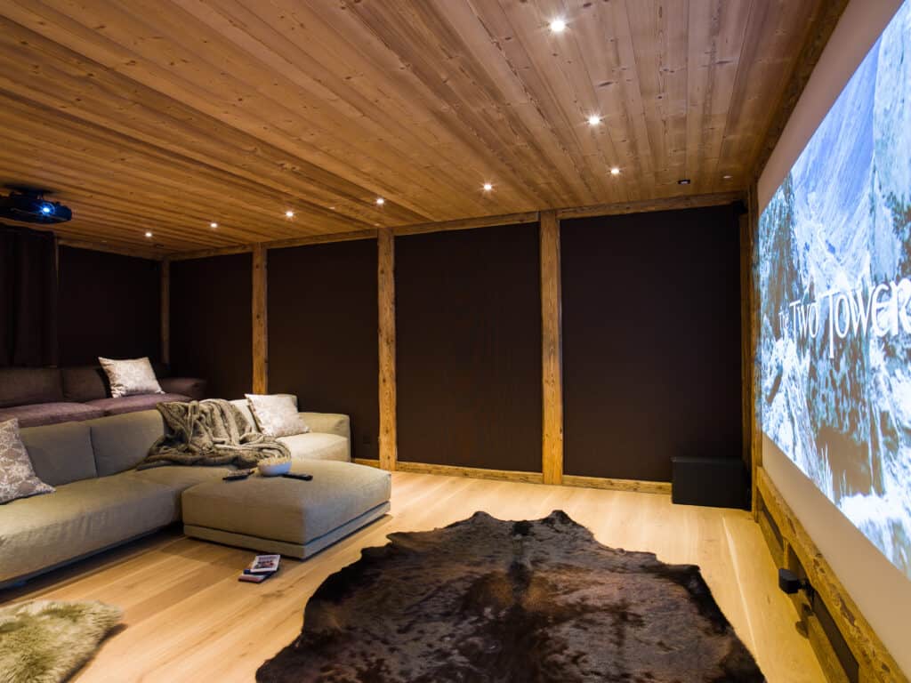A spacious cinema room with dark walls and large grey and purple sofas 
