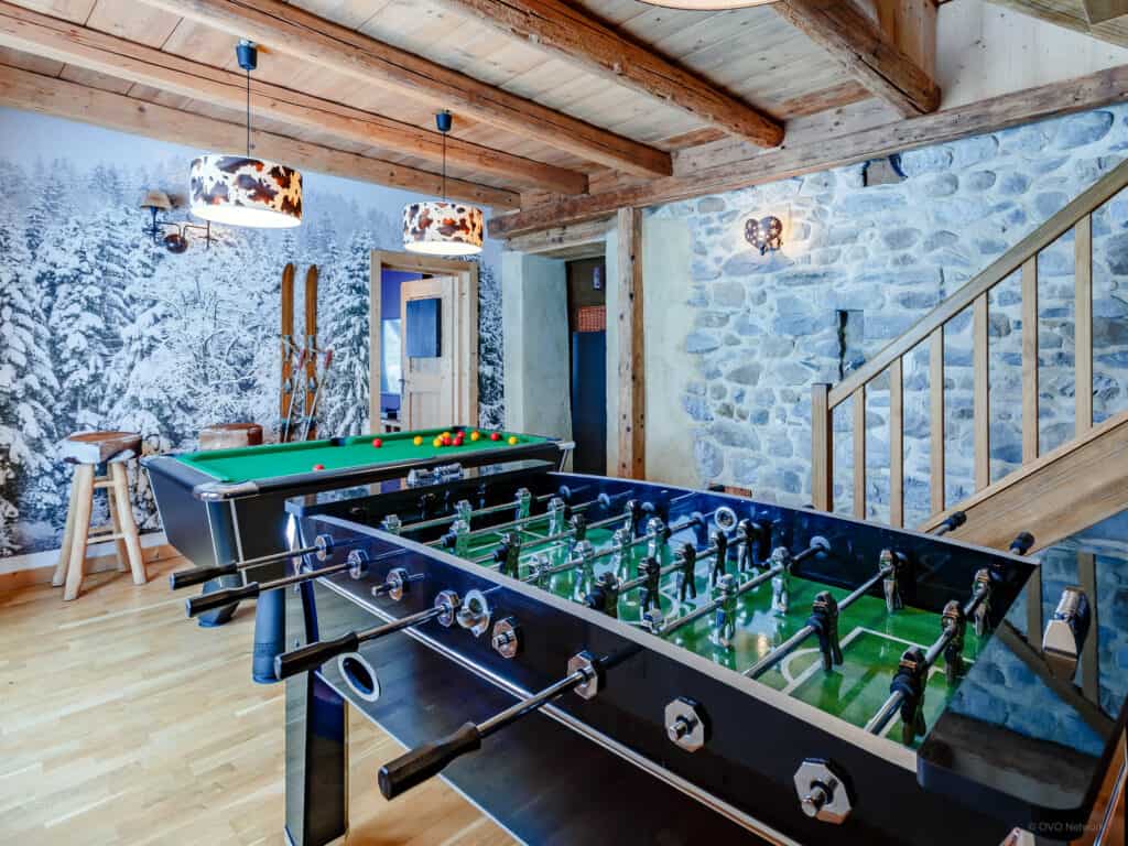A table football and pool table in an Alpine themed room with skis on the wall and cow print deco.