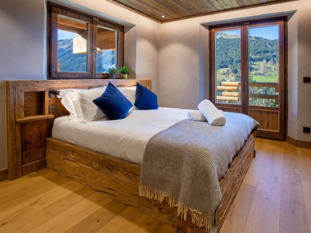 Chambre double boisée avec coussins bleus et linge de lit blanc. Vue montagne
