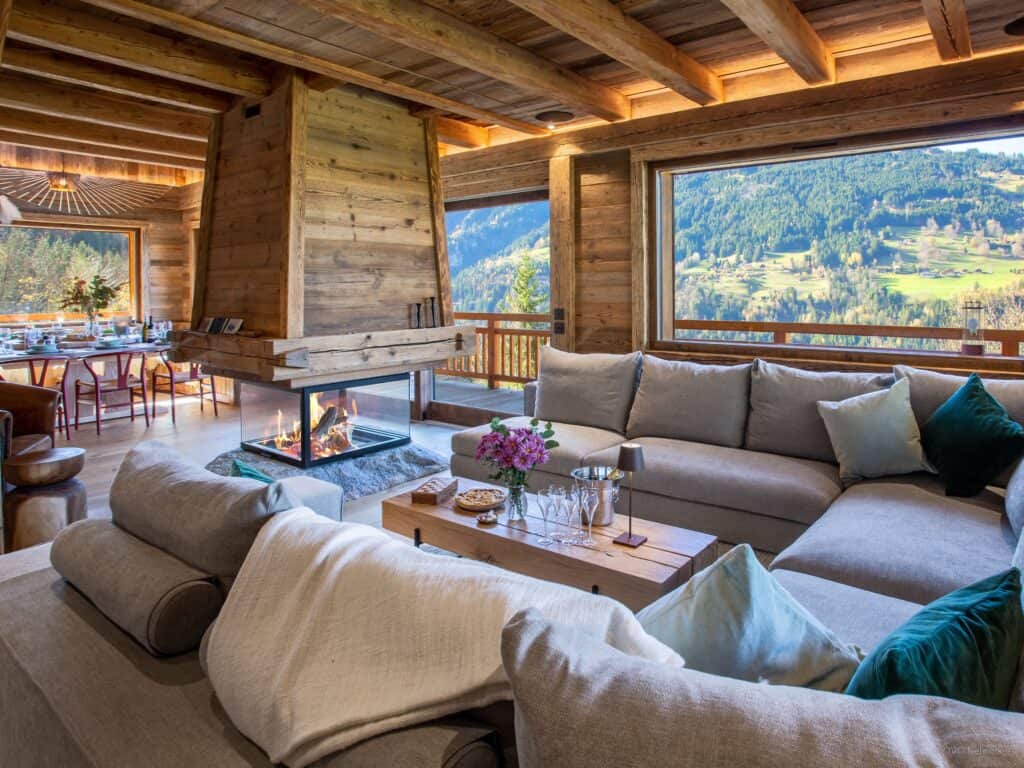 Vaste salon avec large canapés, cheminée et magnifiques ouvertures sur la montagne
