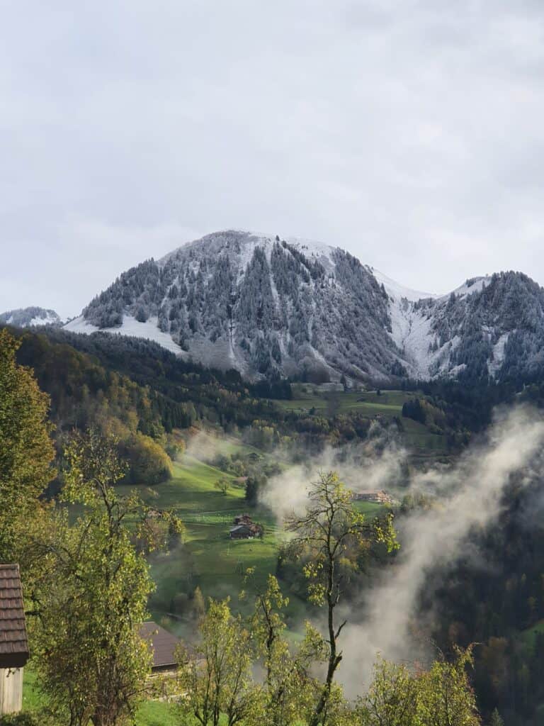 Village de Manigod couvert d'un légère brume. La montagne en arrière plan est couverte de neige.