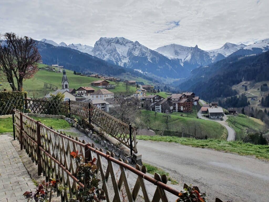Vue panoramique du village de Manigod. L'église et les résidences sont visibles au premier plan. Les montagnes environnantes enneigées constituent l'arrière plan.