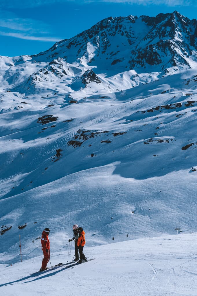 An ESF instructor with two students on a piste in the Trois Vallees. A cable car can be seen in the valley