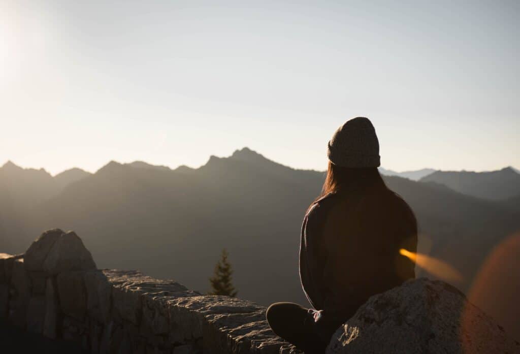 Une femme assise de dos regardant vers la montagne. 