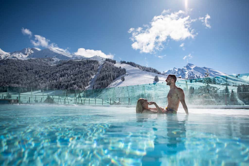 Un couple qui se baigne dans la piscine extérieure du centre aquatique avec une vue imprenable sur les montagnes. 