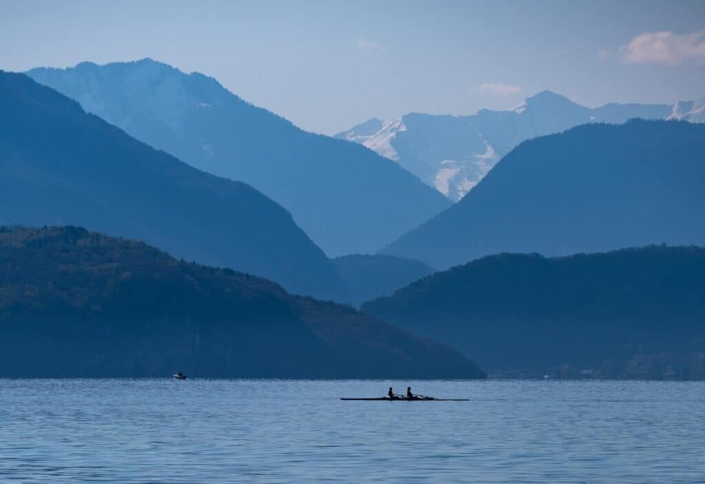 Silhouette de 2 personnes faisant du bateau sur le lac d'annecy. Les nombreux reliefs environnants sont visibles en arrière plan. 