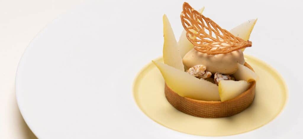 A pear and walnut dessert, topped with a leaf-shaped openwork tuile.