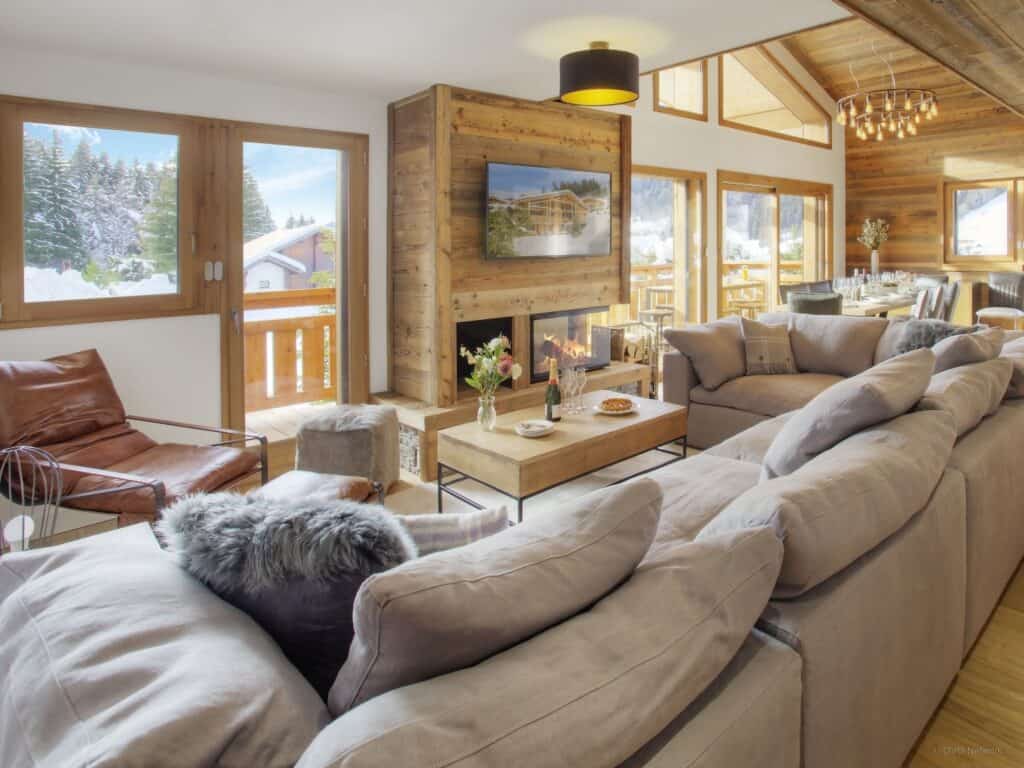 A fireplace is set into the wall in this living room in Chalet Behansa, with a huge sofa and doors on to a balcony