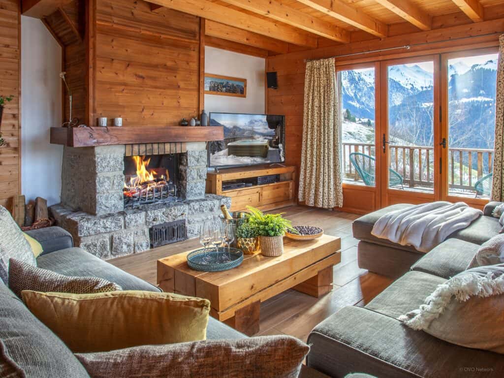 The lounge at Chalet Morclan in Manigod La Clusaz where cosy sofas are arranged around a fireplace and positioned to enjoy the view through the bay windows.