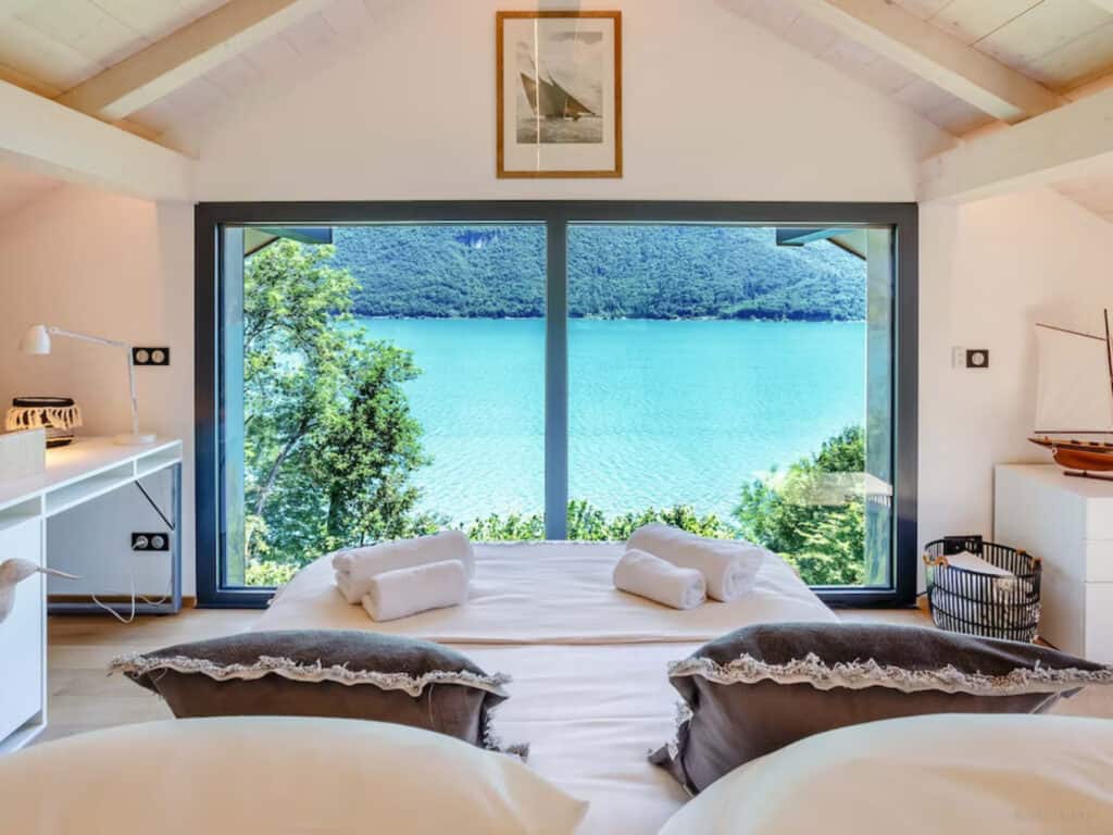 A bedroom with a white double bed and lake view