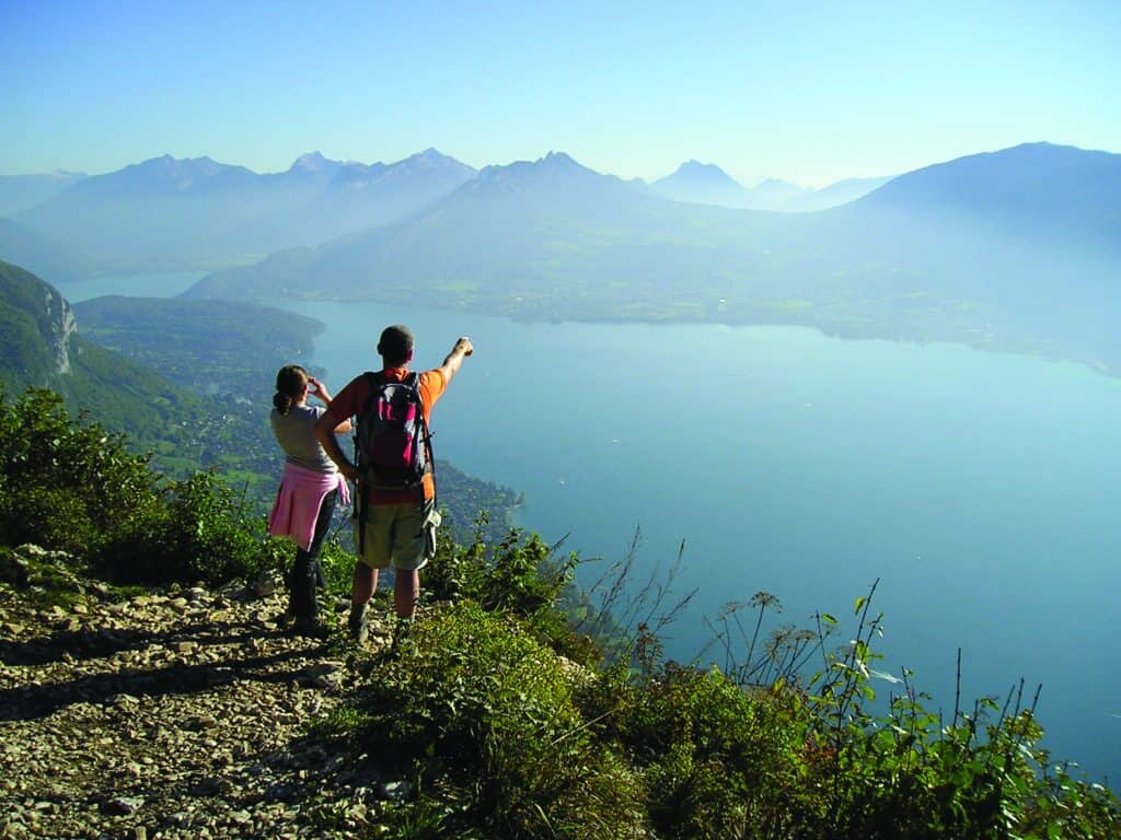 Two walkers enjoy the views across Lake Annecy from the mountains