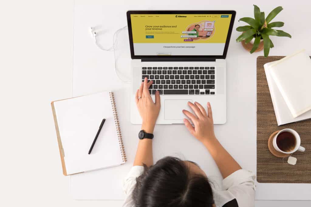 A view from above of a woman sitting at her laptop with a cup of tea and a notepad