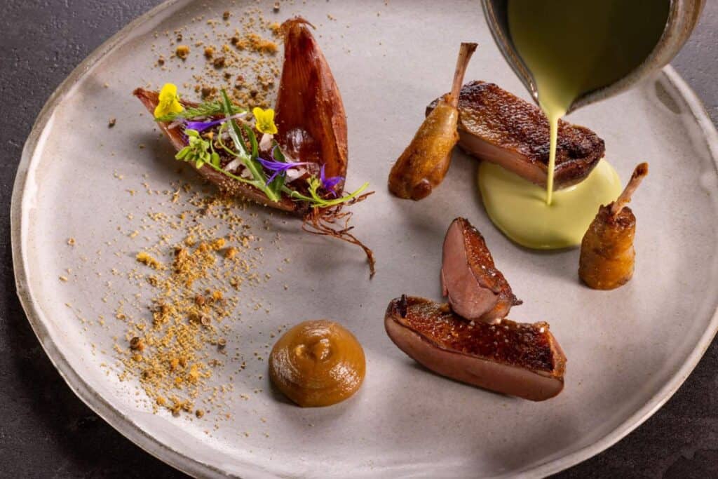 Sauce is added to as beautifully plated dish of duck and garlic
