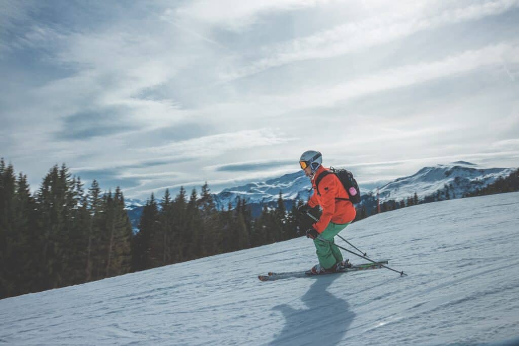 Un homme portant une veste orange et un pantalon vert faisant du ski le long d'une piste. 