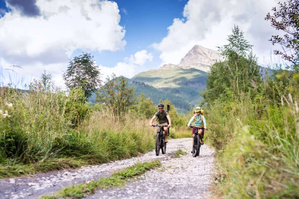 A couple cycle down a mountain path in the sun
