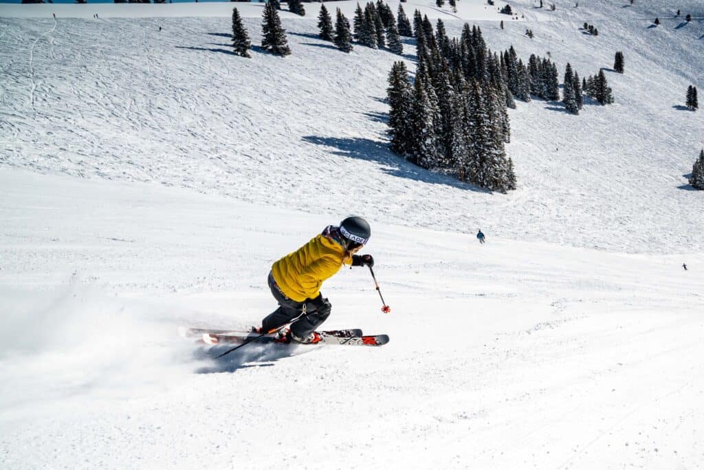 Une personne vue de dos, portant une veste jaune et un  pantalon foncé, faisant du ski. 