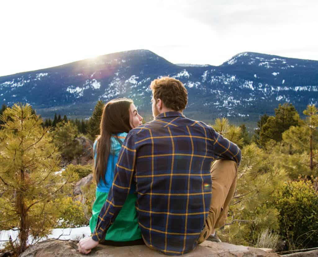Un couple assis côte à côte sur un rocher regardant la montagne au coucher du soleil. 