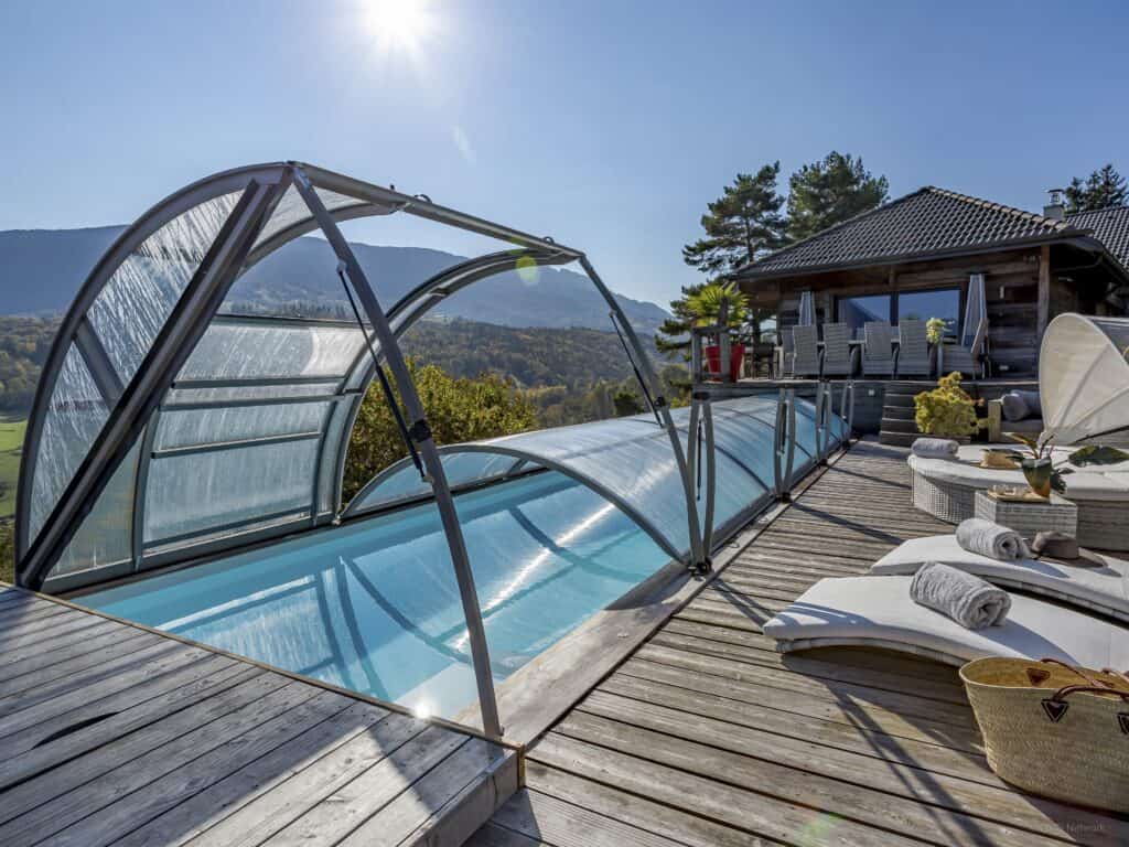 A covered outdoor pool on a sunny terrace furnished with sunbeds