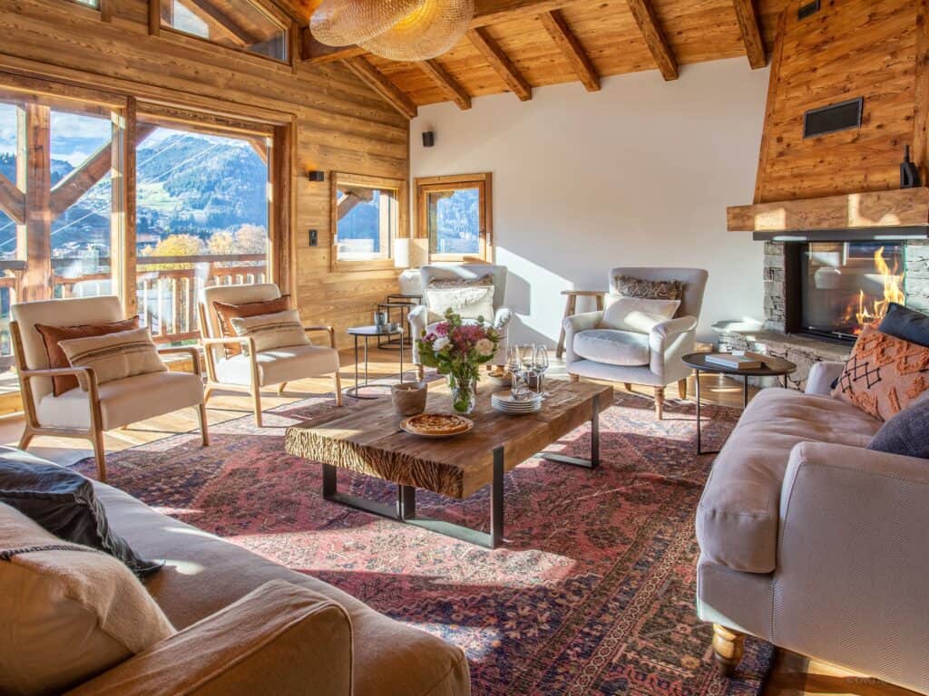 Sunlight streams through the windows into the living area at Chalet Xanadu in Morzine, where cosy sofas and chairs are arranged in front of the fire