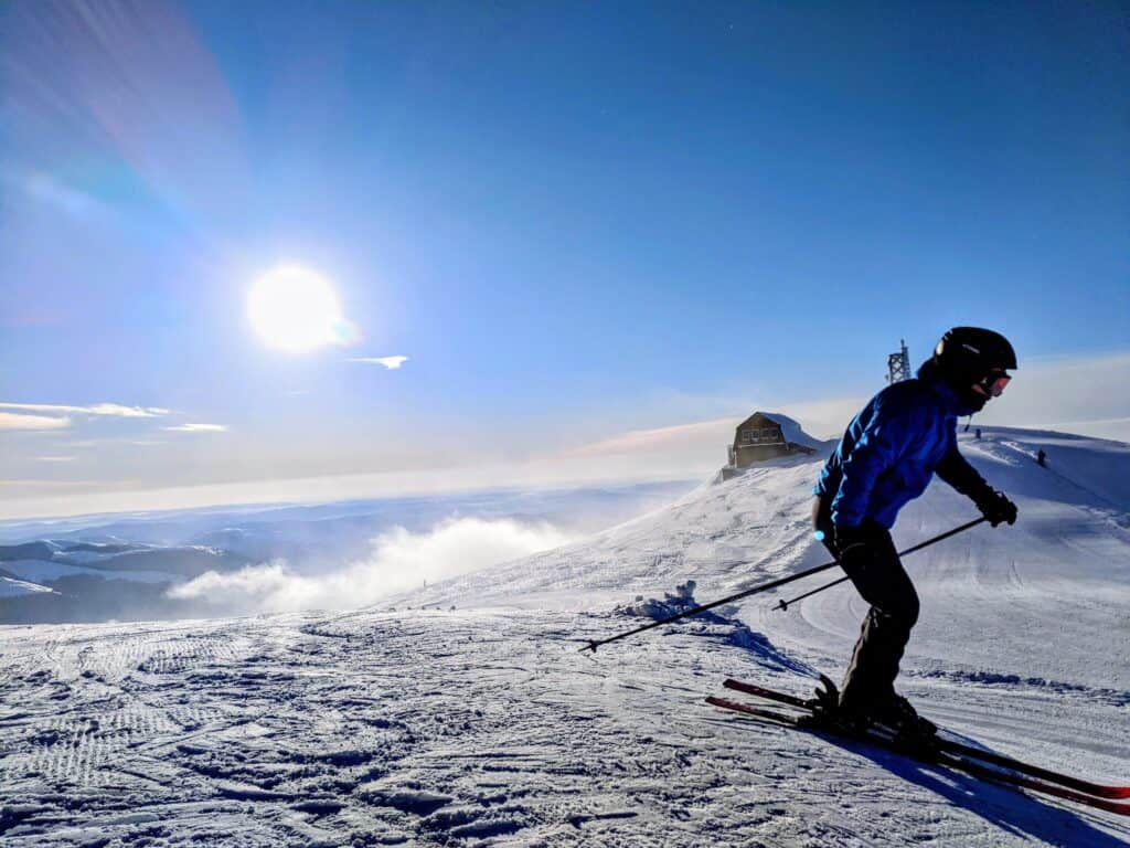 Une personne faisant du ski au coucher du soleil, avec un chalet en arrière plan. 