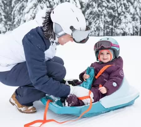A mother straps her child into a sledge using a harness