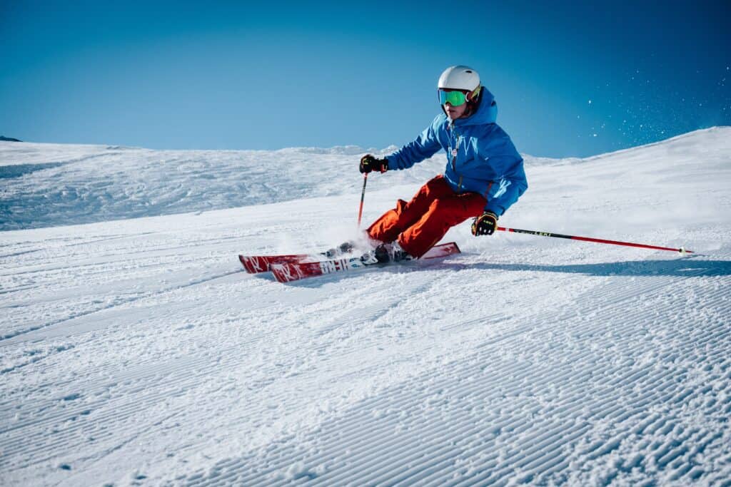 Un homme portant une veste bleue et un pantalon orange descendant une piste de ski.