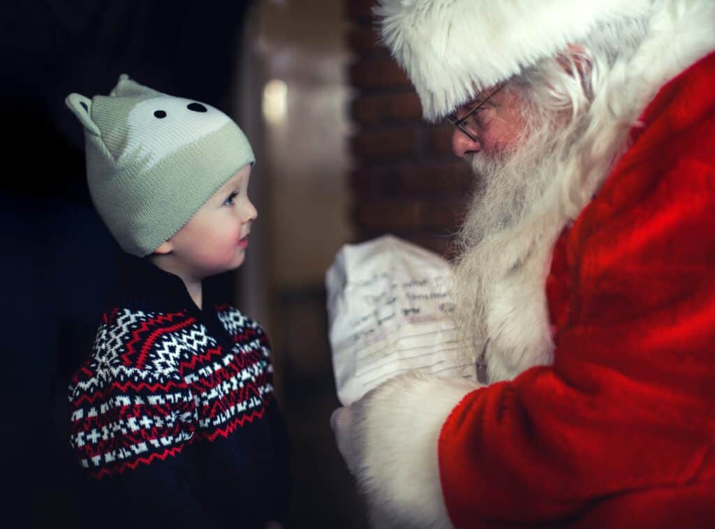 Un petit garçon portant un pull en laine et un bonnet discutant avec le Père Noël. 