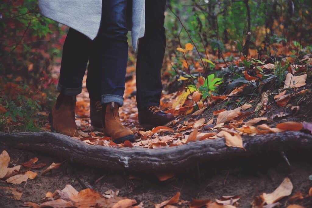 A woman and man's legs are photographed walking through fallen autumn leaves