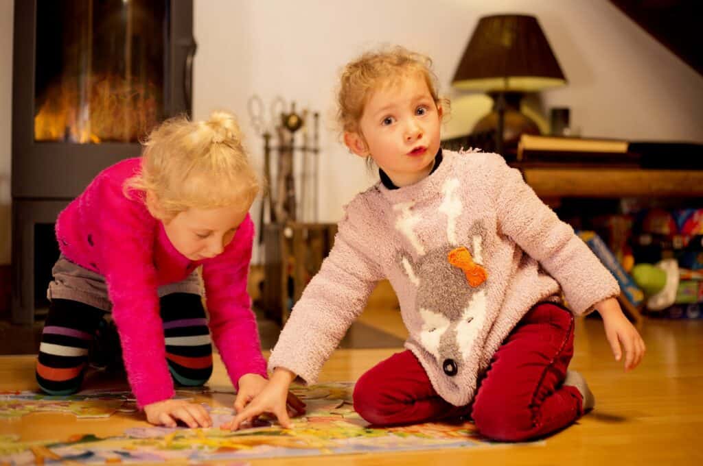 Two young girls play a game in front of the fire at a ski chalet