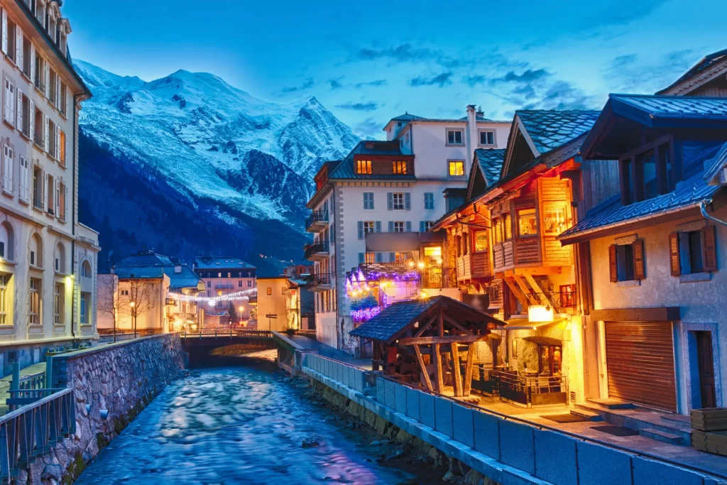 The village of Chamonix, lit up for the evening, with snow peaks behind it