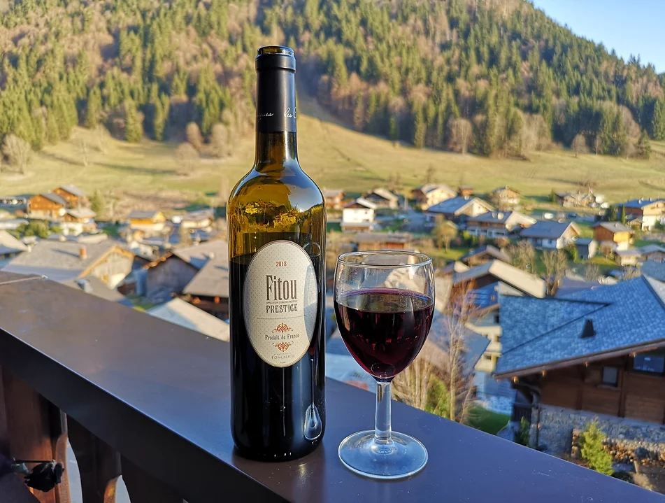 A bottle of French red wine with a glass of wine on a balcony overlooking an Alpine village