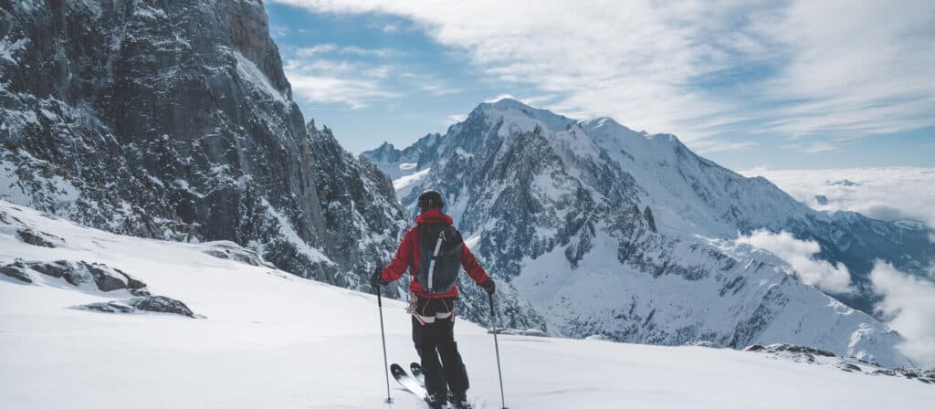 A skier stands on a snowy piste in Chamonix, surrounded by snowy mountains