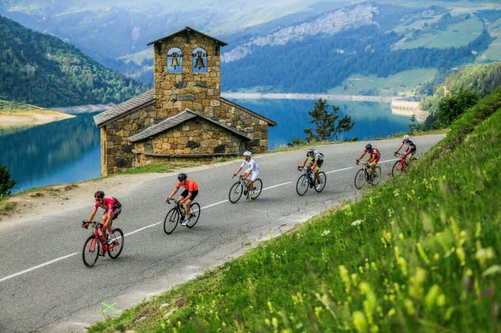 Six cyclists pass a pretty chapel on the edge of a lake