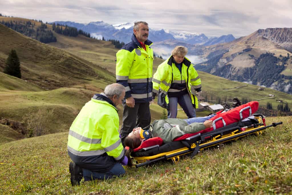 Three rescue medics attend to a woman lying on a stretcher in the mountains