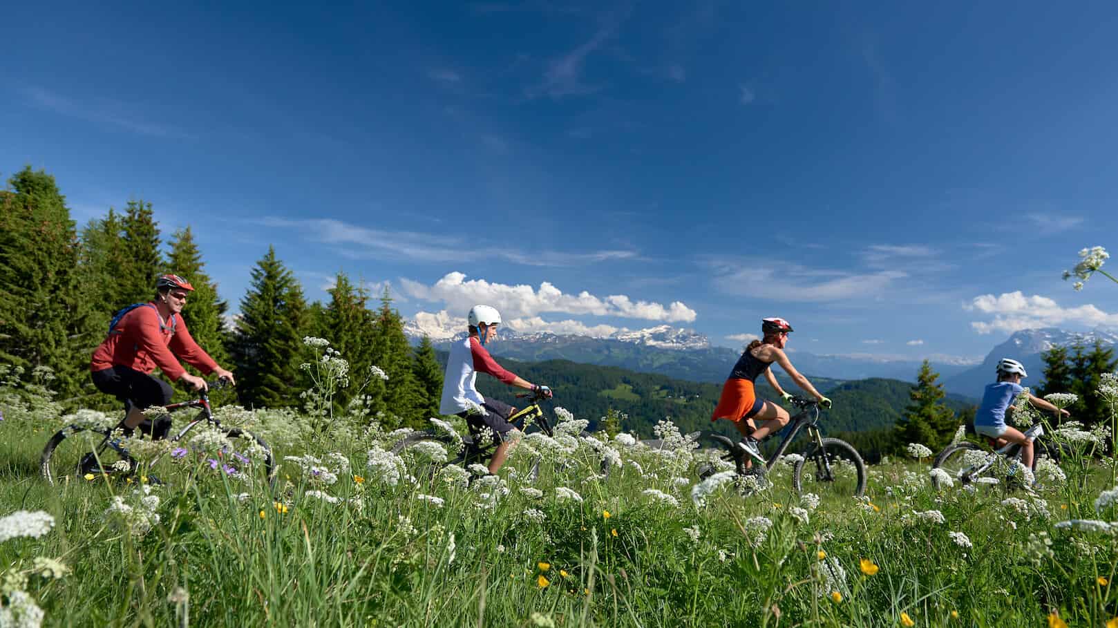 Famille profitant du soleil de la montagne pour randonner en vélo dans la station de ski Les Gets.